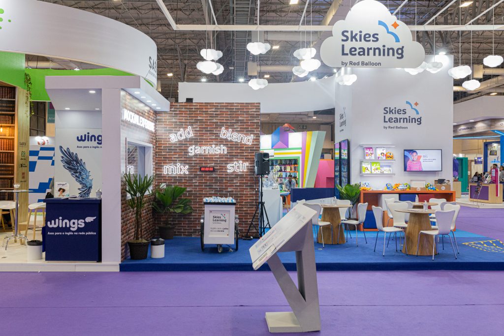Stand da Skies Learning na Bett Brasil 2023, com mesas, cadeiras, televisão, livros e a logo da marca