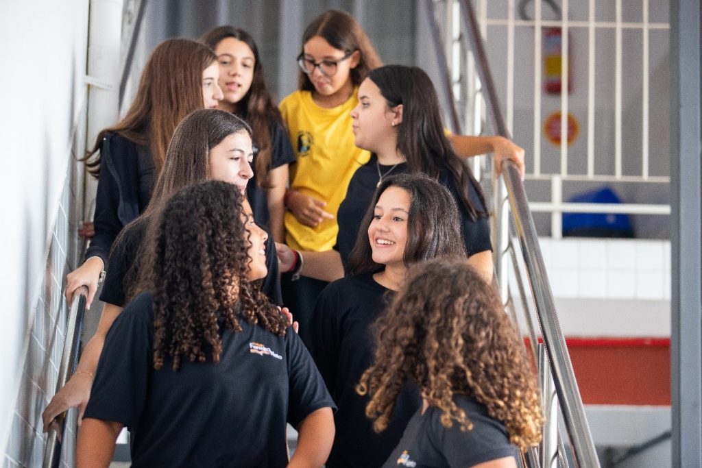 Oito alunas conversando de pé em uma escada, para representar alunos bilíngues